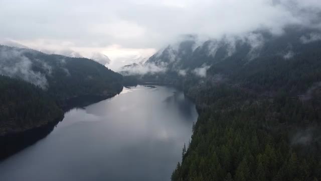 Establishing shot of the lake in between the mountains covered with forest with electricity lines