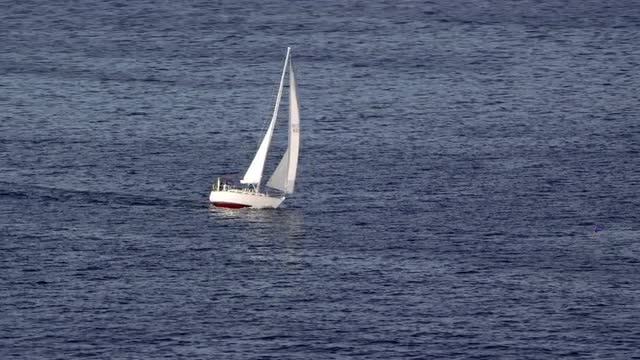WIDE AERIAL around sailboat leaning in wind on water