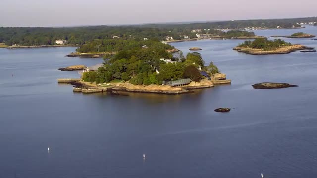 AERIAL POV toward and over small Thimble Islands with houses on them and boats in Long Island Sound