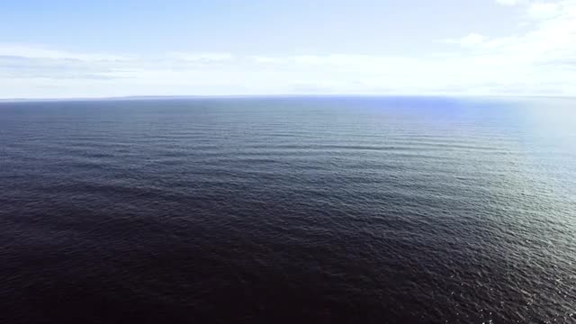 WIDE AERIAL POV over Atlantic Ocean with white clouds in blue sky