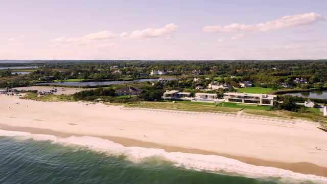 WIDE AERIAL POV with PAN to SIDE POV along coast with mansions on beach