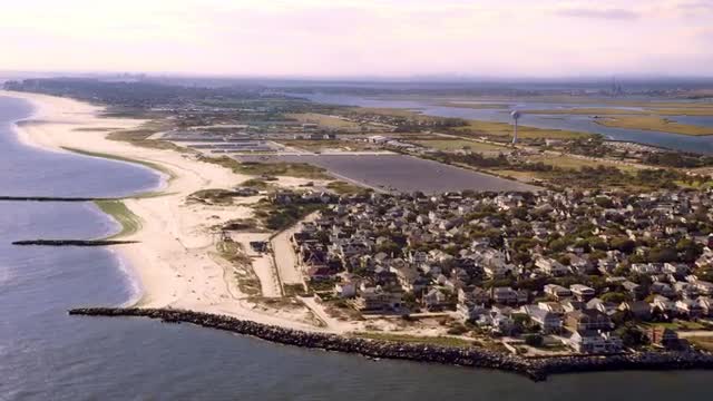 WIDE AERIAL POV over coastal neighborhood of Point Lookout and beach on Long Beach Barrier Island