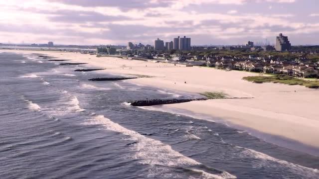 WIDE AERIAL POV past houses along beach with Manhattan skyline way off in the distance, Long Beach, 