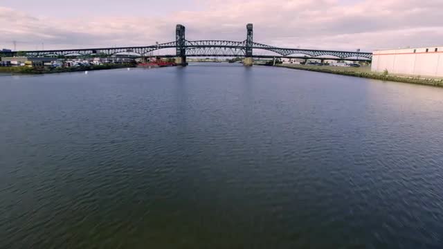 WIDE AERIAL POV up Passaic River lined by industrial plants toward 1/9 bridge then landing on helipa