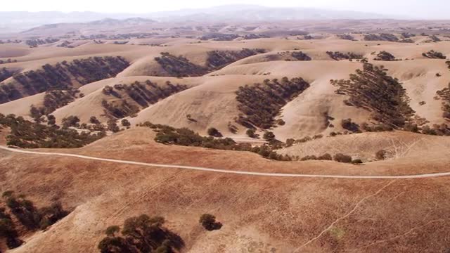 WIDE AERIAL POV over desert mountains with roads and patches of trees, California