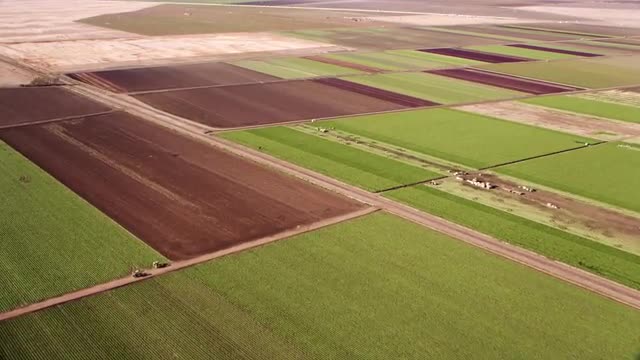 WIDE to MEDIUM AERIAL POV over patchwork farm fields in desert mountain valley, California