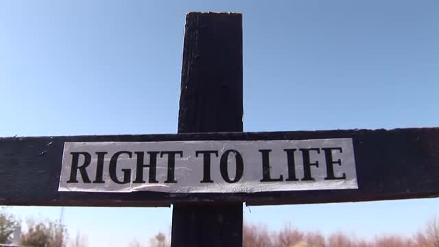 A wooden cross has a "Right to Life" banner attached.