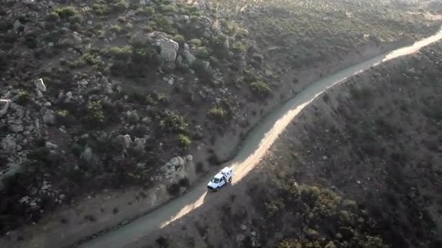 Aerial view of a border patrol vehicle on a rocky dirt road.