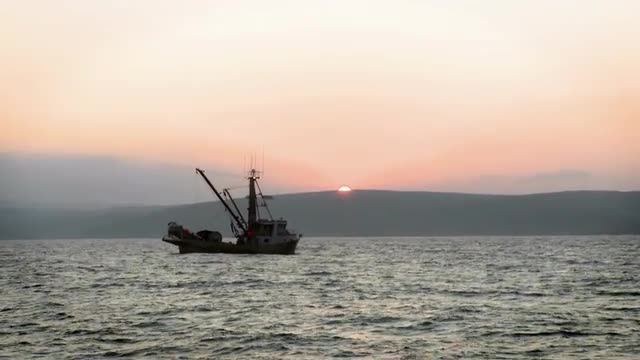 Two boats are sitting in the water as the sun sets over the mountains.