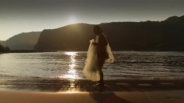 A gorgeous shot as a fisherman walks in front of the sunset with his net in slow motion.