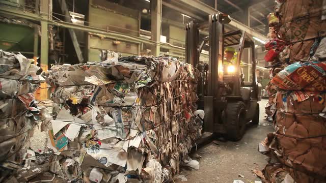 A skip loader moves pallets of recycled materials in a factory.