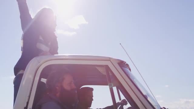 A couple stands in the bed of a pickup truck as it drives along a rural road.