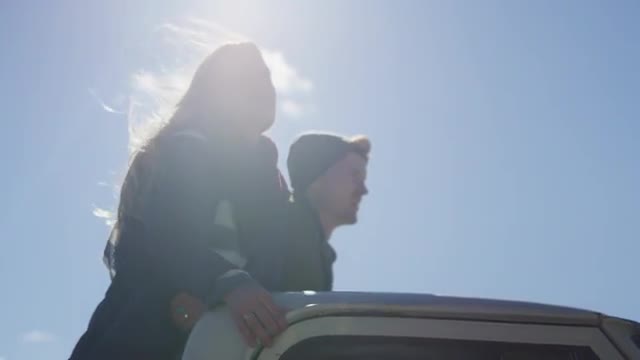 A couple stands in the bed of a pickup truck as it drives along a rural road.