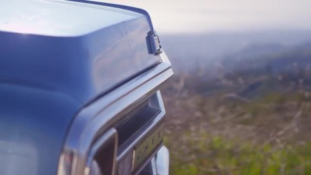 Close-up of the front of a blue pickup truck as it drives along a rural road.