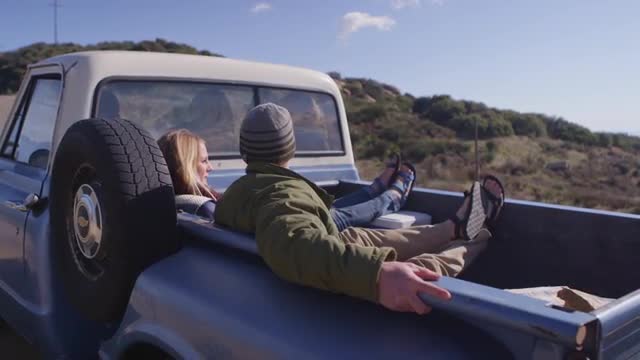 A couple sits in the back of a pickup truck parked on a rural road.