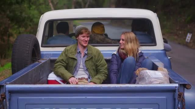 A couple sits in the back of a pickup truck as it pulls away.