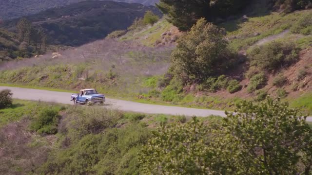 A blue pickup truck drives on a rural road.