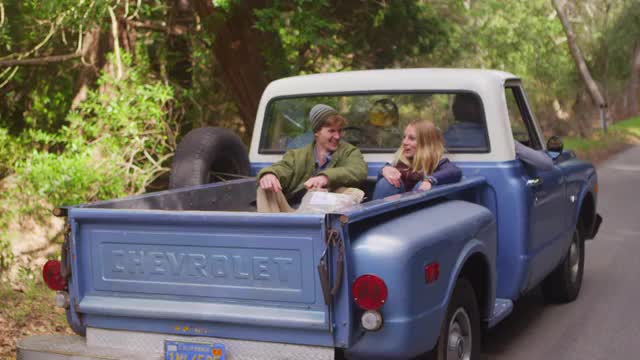 A couple sits in the back of a pickup truck as it pulls away.