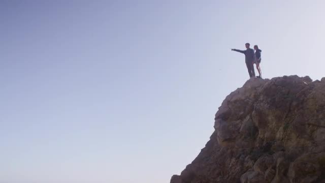 Wide view of a couple standing atop a sea cliff.