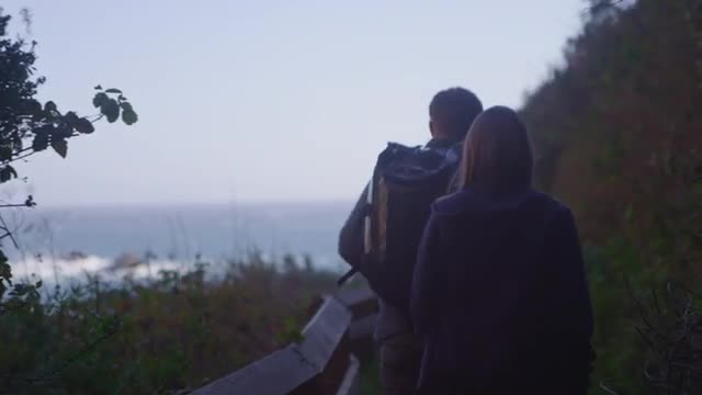 A couple walk along a path on a sea cliff.