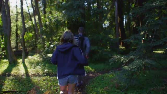 A couple run down a path in a forest.