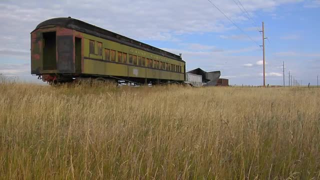 An old abandoned Pullman railway car sits in a field on a lonely stretch of railroad track.