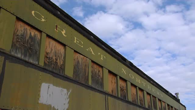 An abandoned "Great Northern" railway car sits in front of a blue sky and clouds.