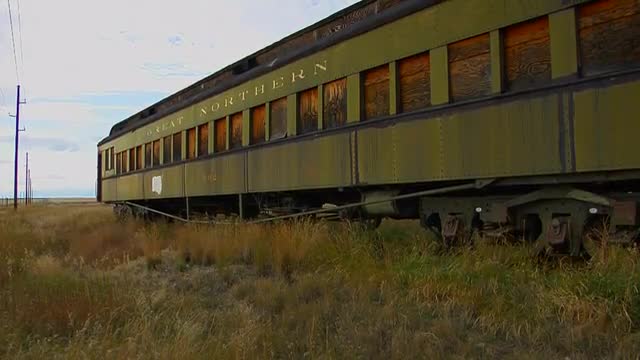 An old abandoned Pullman railway car sits in a field on a lonely stretch of railroad track.