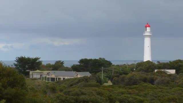 A white and red light house stands near the ocean.