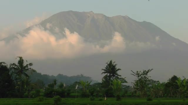 Clouds move slowly in front of a tall mountain range.