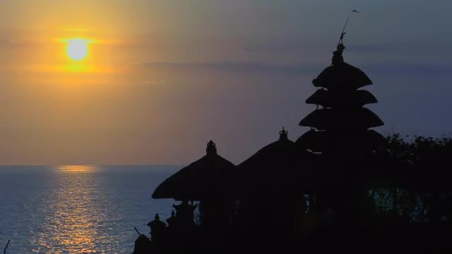 The sun silhouettes The Pura Tanah Lot temple during golden-hour.