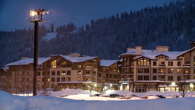 A snowplow passes in front of a hotel in a mountain resort.