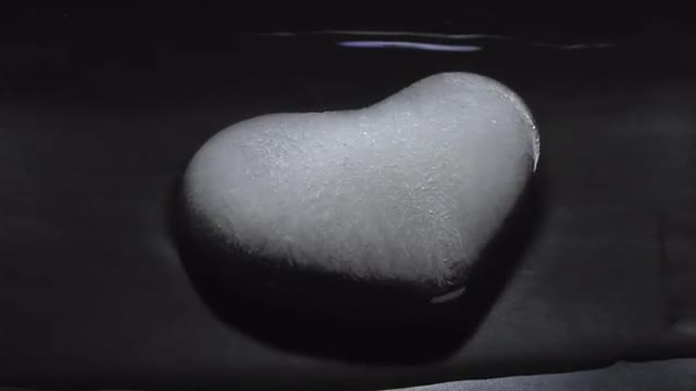 An ice heart melts on a dark surface