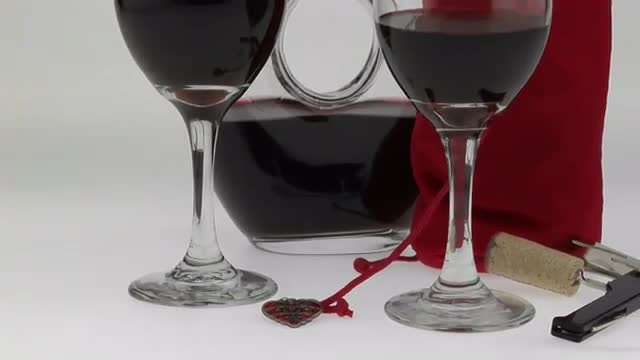  glasses filled with red wine and surrounded by a half-full carafe and red velvet bag are displayed 