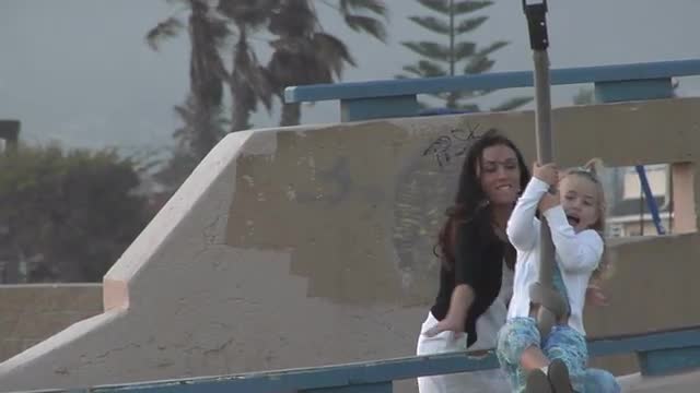 A mother helps her daughter hang on to a zip-line then watches her as she rides away laughing.