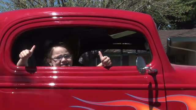 A young girl gives two thumbs up out a car window.