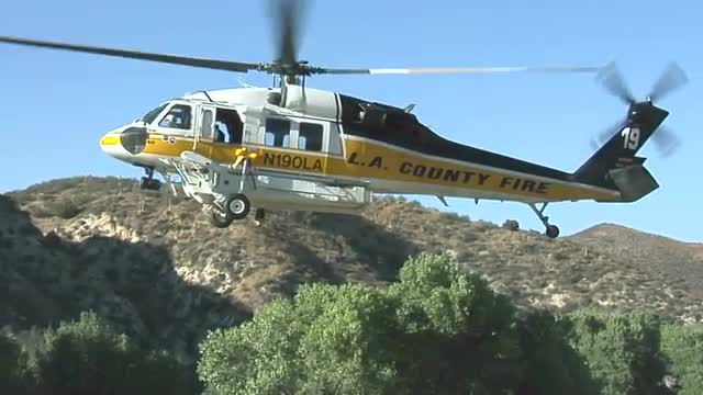A fire fighting helicopter draws water in a mountain clearing.