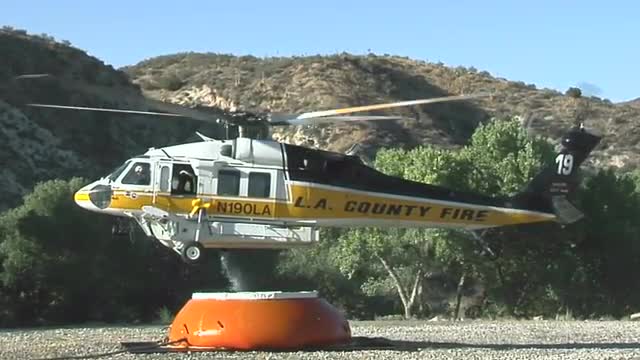 A fire fighting helicopter draws water in a mountain clearing.