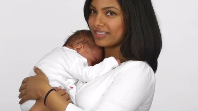 Happy mother smiles for the camera as her baby sleeps in her arms