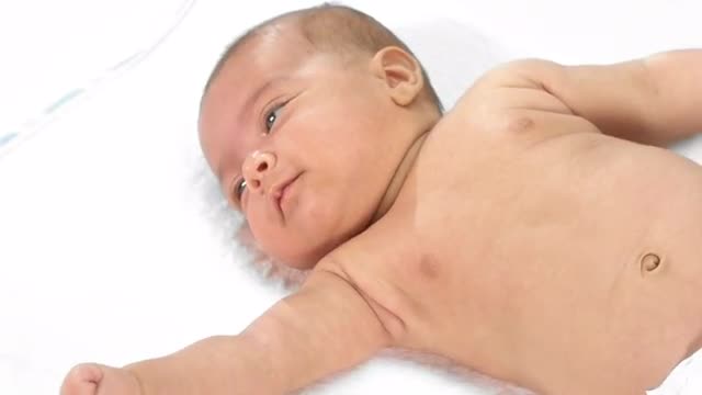 An adorable newborn baby rolls around on her back on white