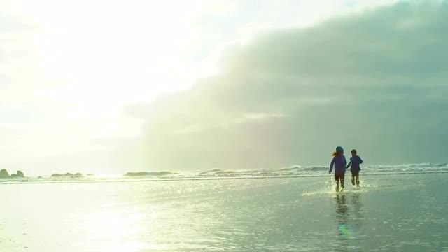 Two kids run through the water at the beach towards the camera in winter
