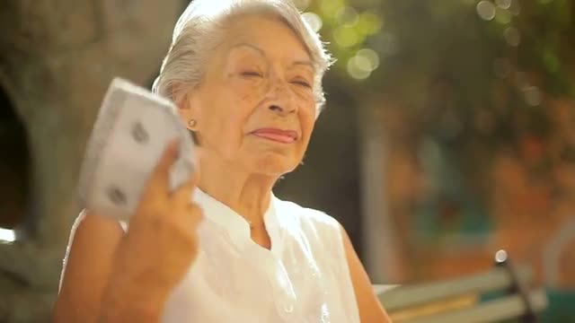 An old lady sits on a bench and fans herself in the heat