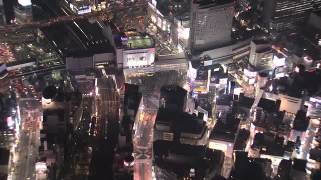 Aerial zoom in illuminated Shibuya scramble crossing night people Tokyo 