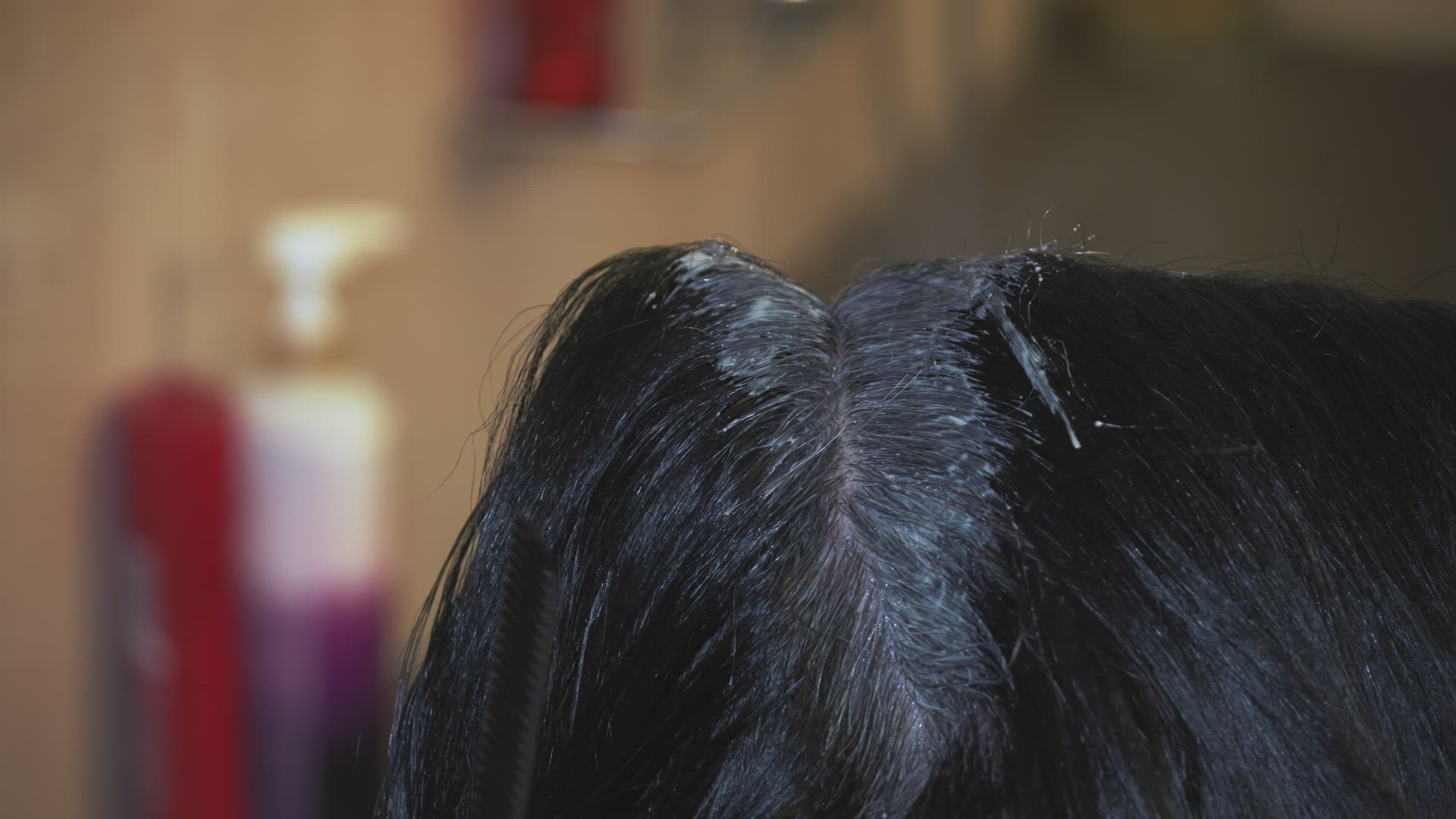 Hair dye color applied on the scalp by a hairdresser wearing black rubber gloves.