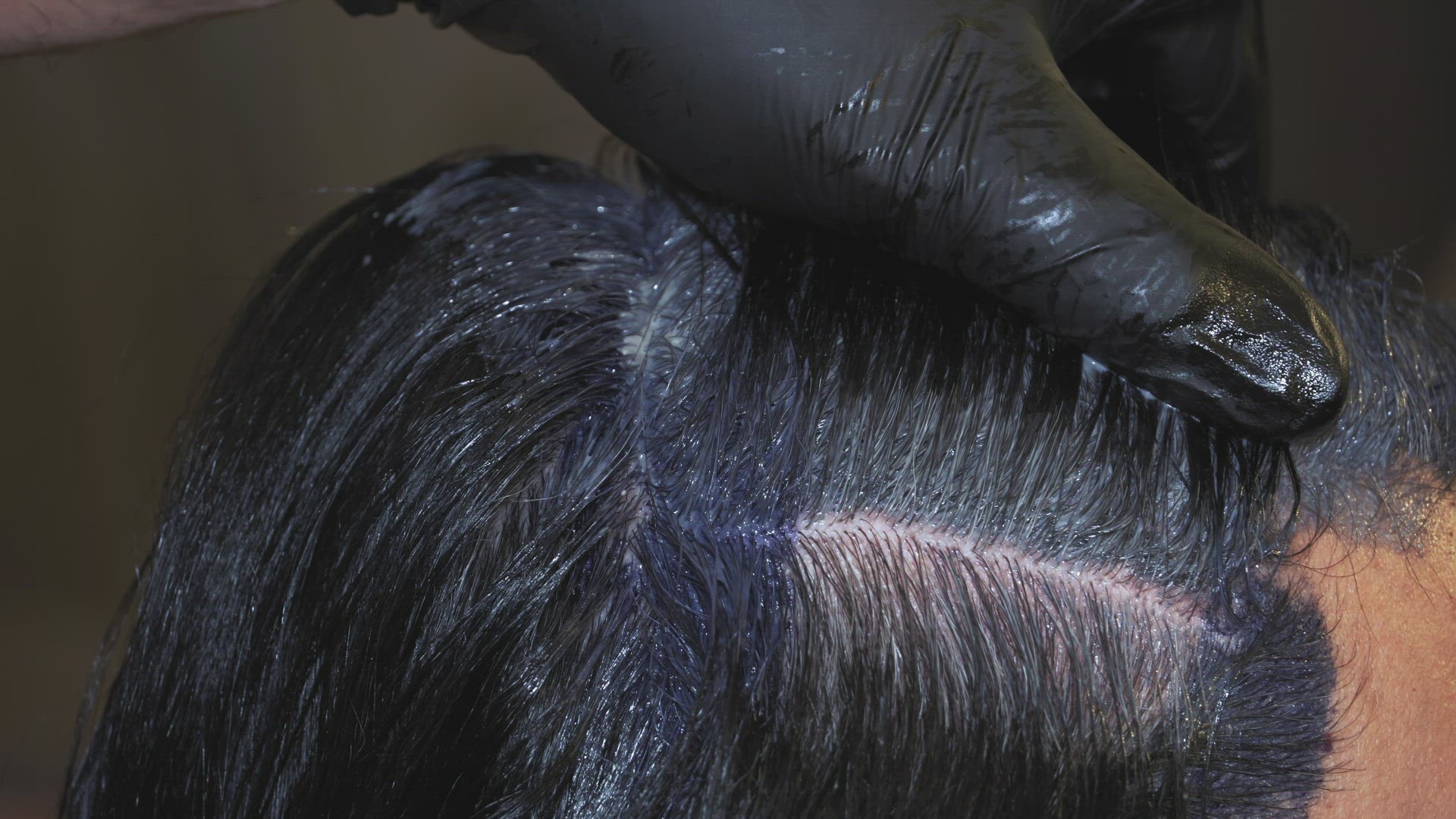 Hair dye color applied on the scalp by a hairdresser wearing black rubber gloves. 