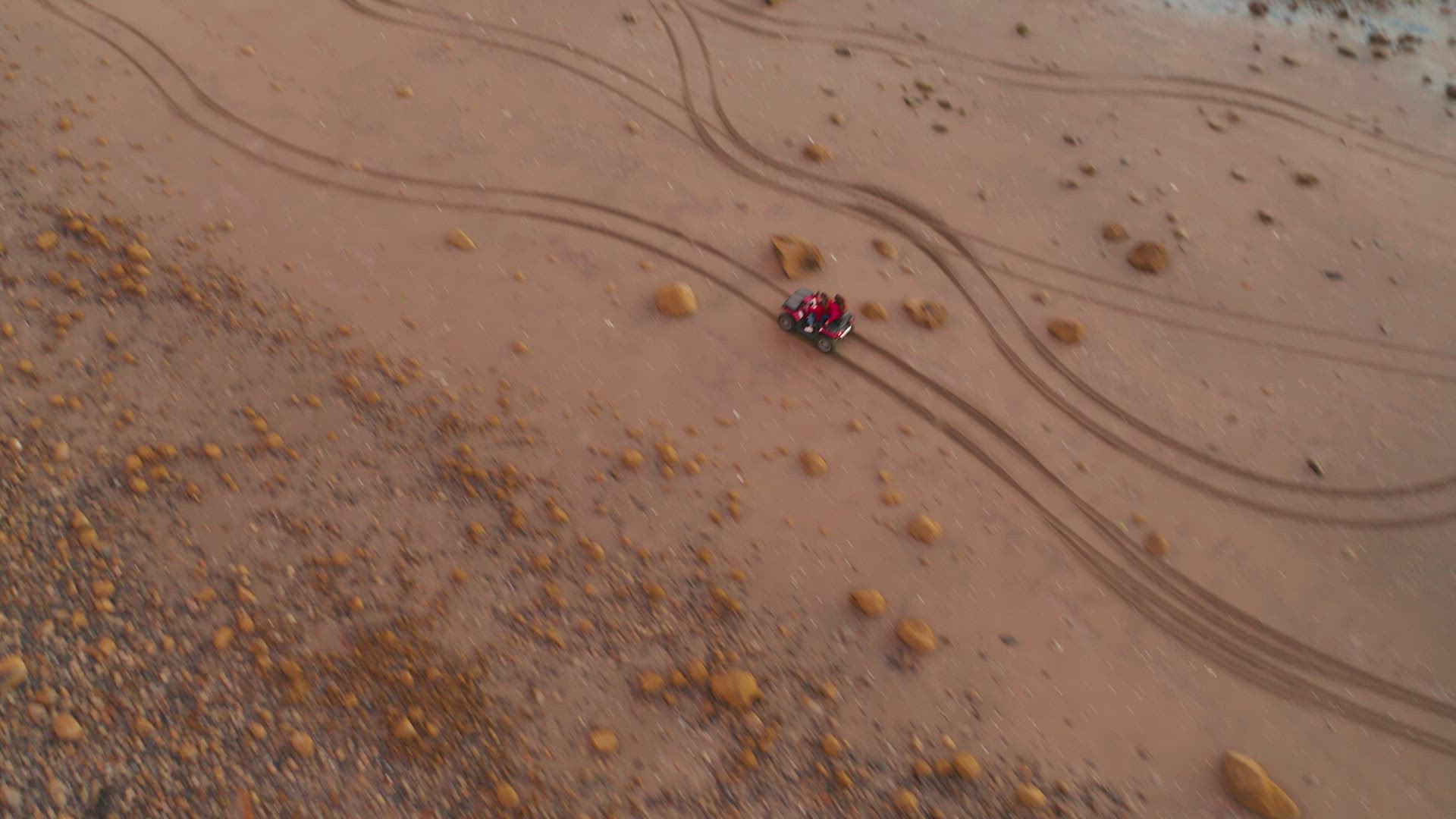Aerial top down shot following a quad bike riding fast along rocky beach at low tide