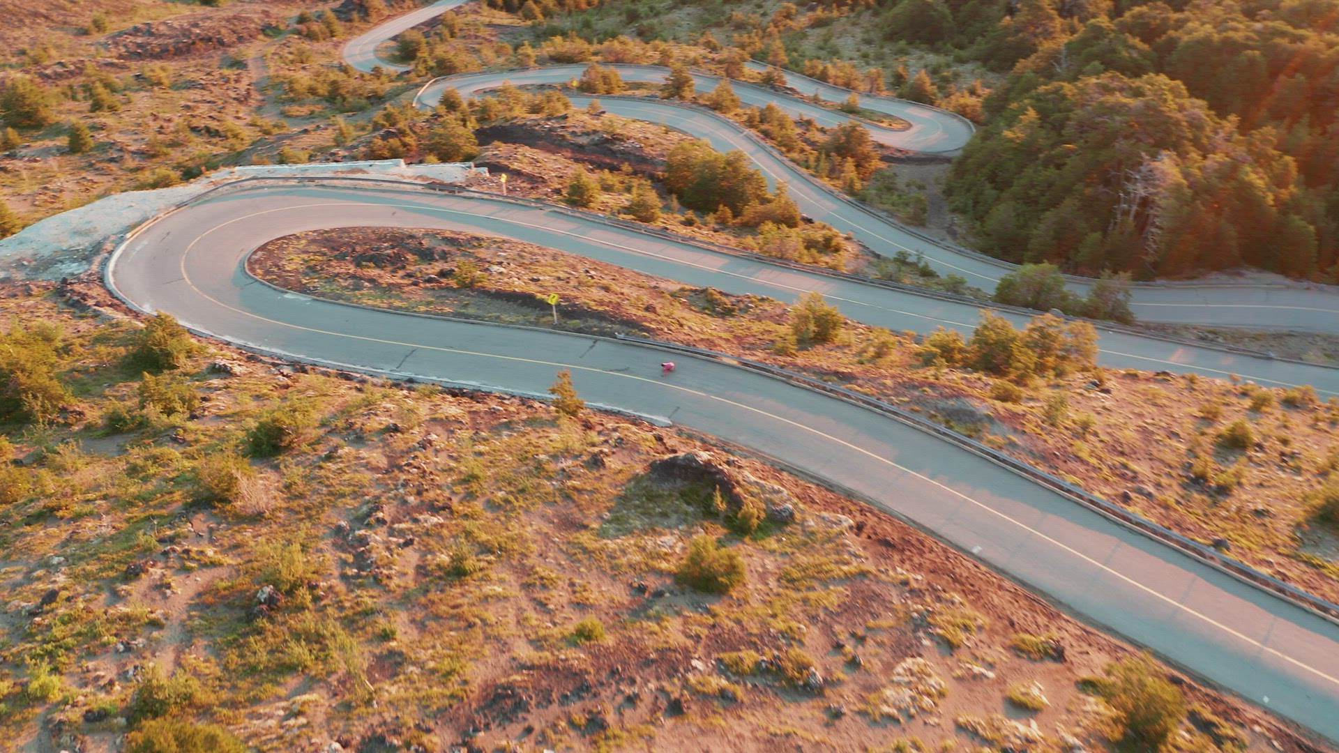Aerial view following a longboard rider on a countryside road with a series of sharp hairpin bends, 