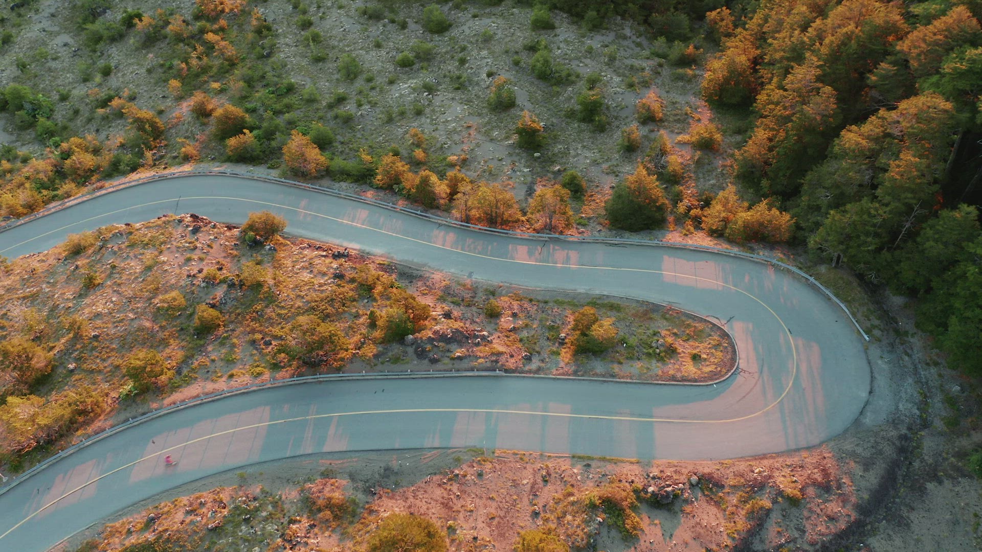 Aerial top view of a mountain road with sharp hairpin bend, longboard rider and car in shot