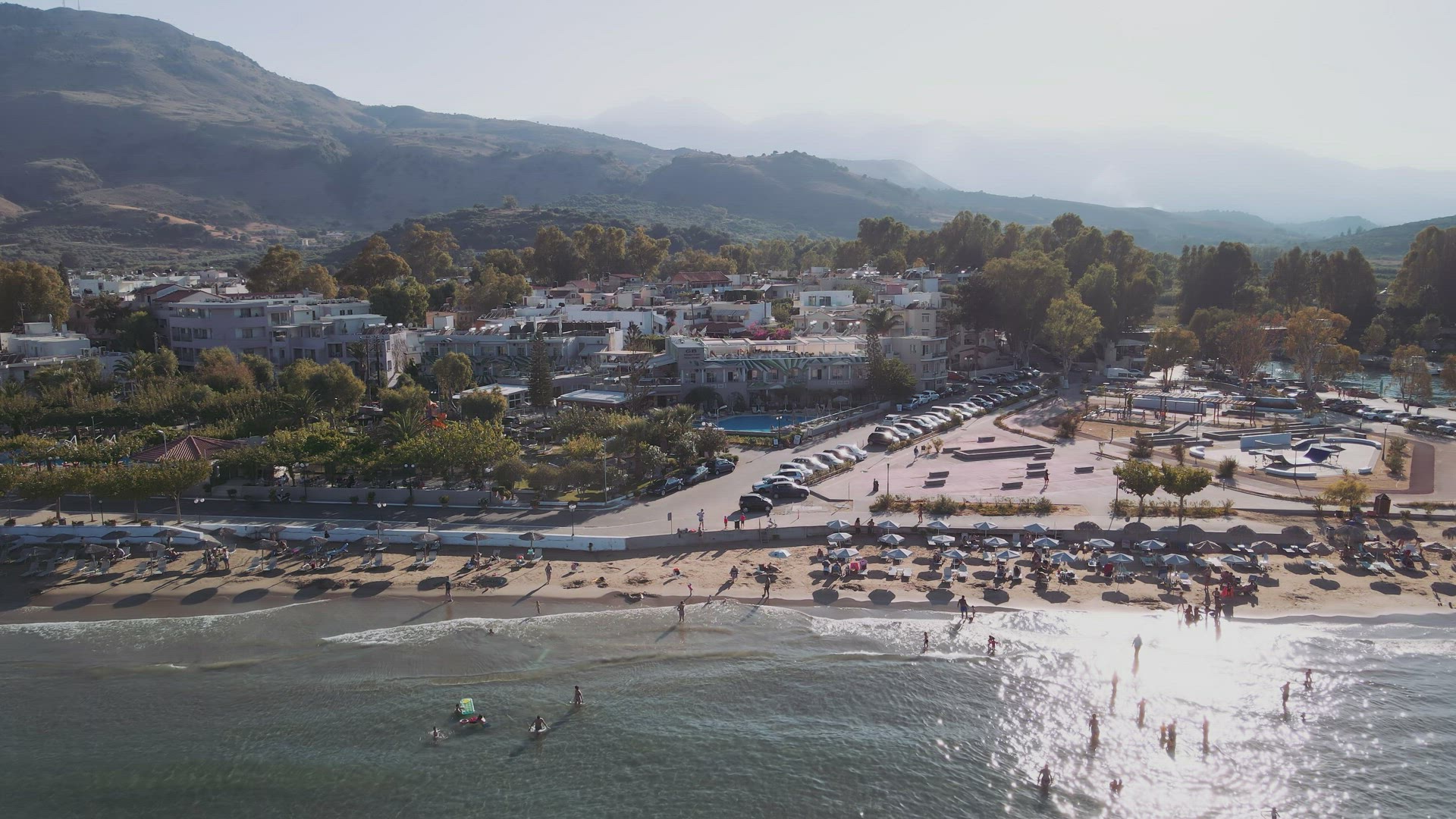 Mediterranean terrain Greek beach bar landscape drone pan shot with unidentifiable bathers. 