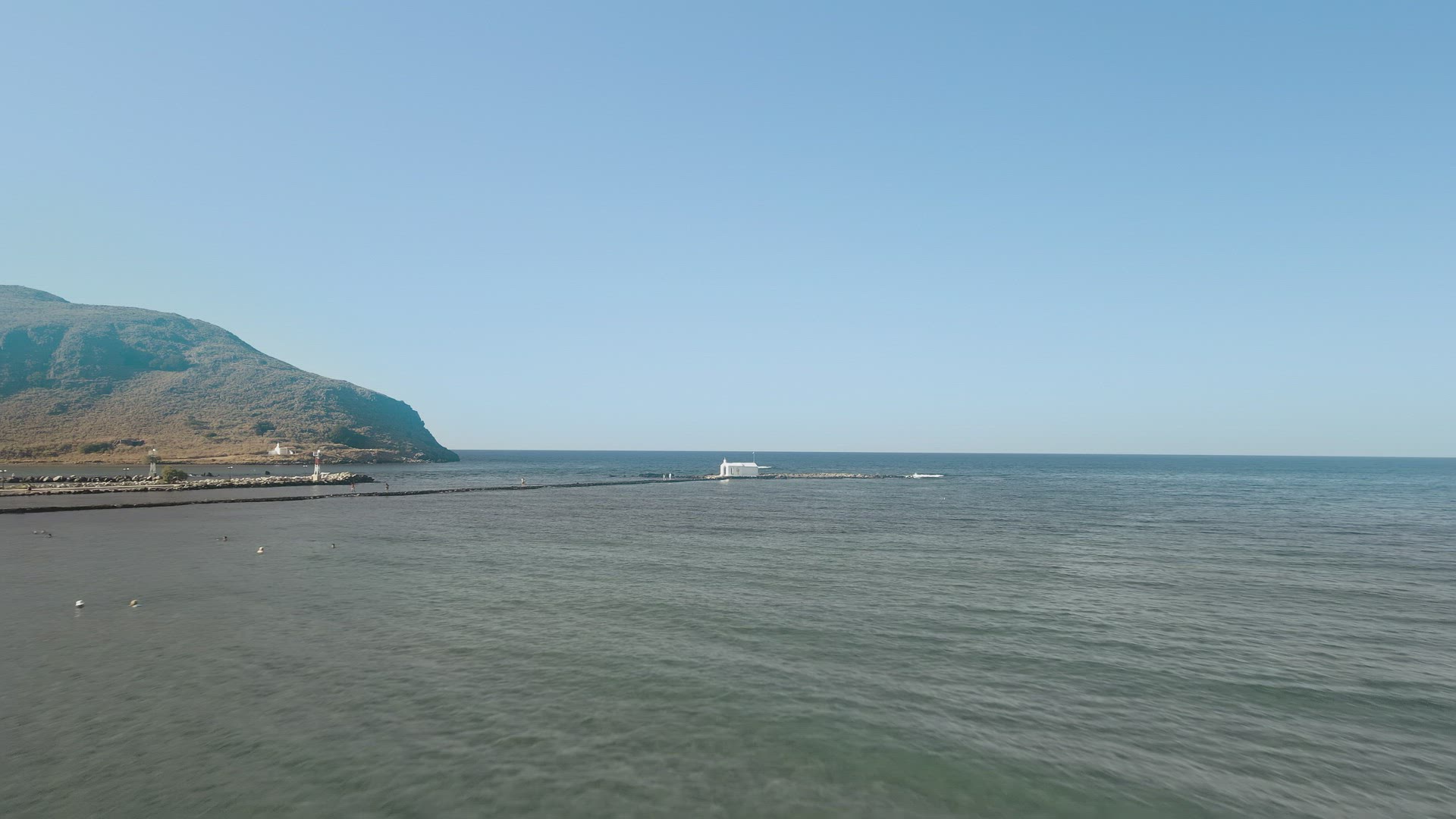 Aerial day view of whitewashed Greek Orthodox chapel around calm sea. 